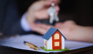 A house model, pen and paper and a person showcasing a real estate ownership