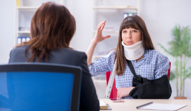 A woman with a neck brace is positioned at a desk, and a lawyer managing her injury situation.