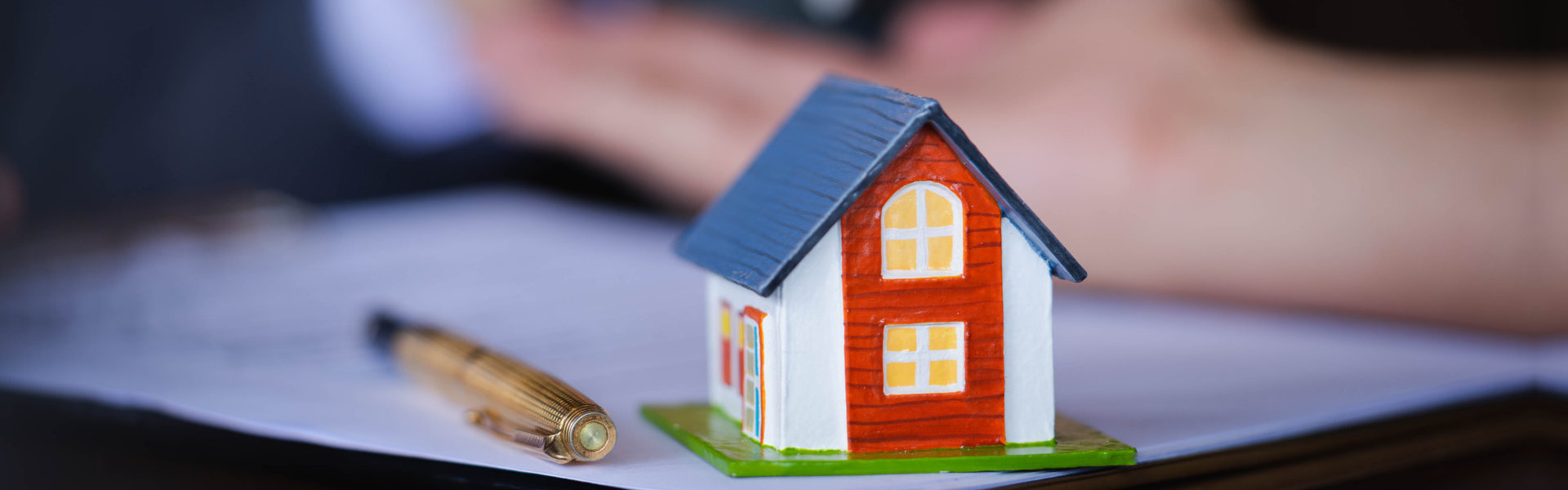 A house model, pen and paper and a person showcasing a real estate ownership